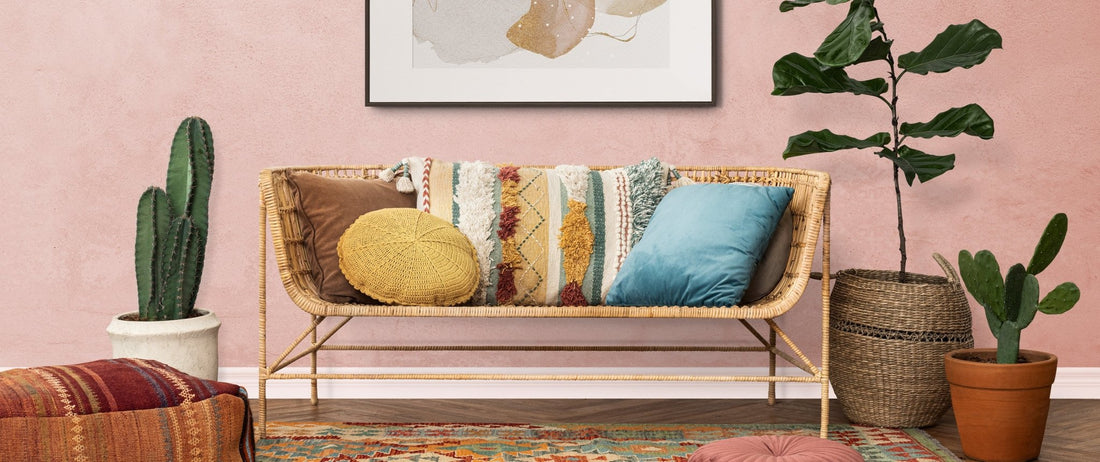 In this image is a bohemian style couch made of natural wicker. There are bright and bold pillows placed on the couch. Everything is in the warm palette of the bohemian style of earth tones.